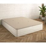 Canapé con un diseño moderno de color beige claro. La estructura es de madera clara y tiene pequeños orificios de ventilación en la tapa, lo que mejora la transpirabilidad. La habitación tiene suelos de madera en tonos cálidos y una planta en una esquina que añade un toque natural al ambiente minimalista.