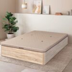 Canapé cerrado de estilo moderno, con una estructura de madera clara y una tapa de color beige con pequeños orificios para la ventilación. El ambiente de la habitación es cálido, con una decoración minimalista que incluye una planta verde, cuadros en la pared y lámparas colgantes.