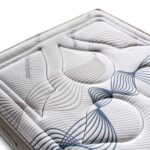 Superficie acolchada de un colchón con un diseño ondulado en relieve, que combina tonos beige y azul oscuro. Las líneas en espiral y curvas dan una apariencia moderna y elegante. El material se aprecia suave y adaptable, con la palabra "Viscoelastic" impresa en varias zonas del tejido, lo que sugiere que es un colchón de alta calidad diseñado para ofrecer confort y adaptabilidad.