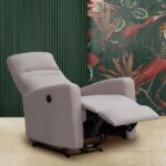 Sillón reclinable en color beige claro, con botonera para una apertura motorizada, en posición extendida. Ubicado en una sala de estar con paredes verdes decoradas con un mural de motivos naturales. Fabricado con tela antimanchas para fácil mantenimiento, ideal para añadir estilo y confort al hogar.