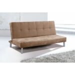 Un sofá cama en color beige con patas metálicas, colocado en una habitación luminosa. El respaldo tiene un diseño acolchado con costuras visibles, y el sofá está sobre una alfombra mullida de color claro. El estilo es sencillo y moderno, ideal para espacios pequeños.