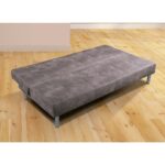 Una cama baja en color gris con patas metálicas, situada en una habitación con suelo de madera. La cama tiene un diseño simple y una textura acolchada, con líneas visibles que indican donde se pliega para transformarse en sofá.