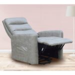 Sillón ergonómico reclinable en color gris claro, con tapicería en tela antimanchas Aqualine Magnolia. Equipado con un sistema Power Lift para facilitar la elevación y reclinación, ideal para personas con movilidad reducida. Incluye un bolsillo lateral para guardar el mando y un mecanismo de apertura con muelle en el asiento para mayor confort. Perfecto para un salón moderno con suelo de madera y lámpara de pie.