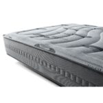 Colchón de perfil bajo con una textura visible en la superficie, que incluye patrones ondulados. El material exterior parece ser de tejido elástico (stretch) en color gris, con un diseño que parece proporcionar ventilación. También se notan detalles acolchados y costuras laterales para mayor soporte.